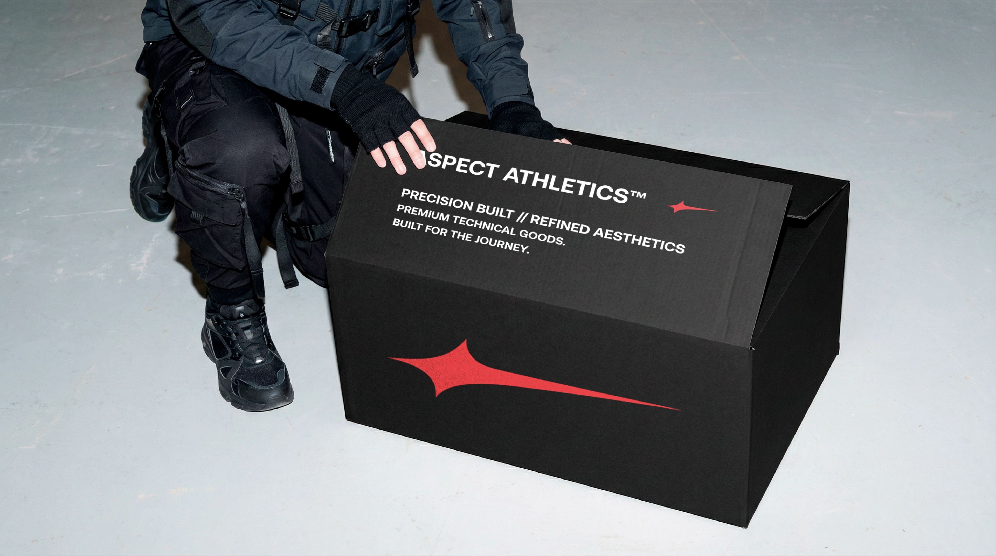 A person dressed in black techwear crouching next to a premium black shipping box for Aspect Athleti